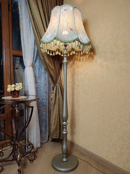 A Victorian floor lamp with a fabric shade and an exquisite floral umbrella motif with tassels.