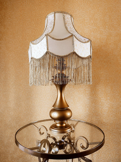 Gold-colored table lamp with elegant lace details and tasseled fringe. 7202