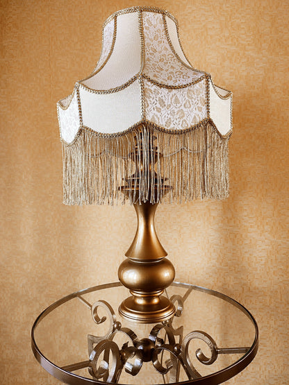 Gold-colored table lamp with elegant lace details and tasseled fringe. 7202