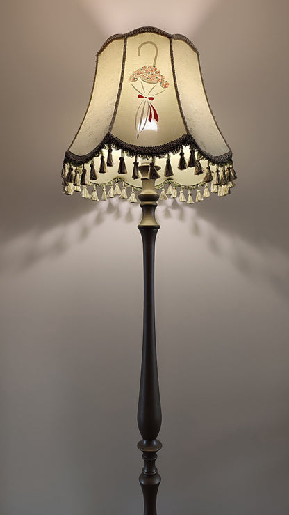 A Victorian floor lamp with a fabric shade and an exquisite floral umbrella motif with tassels.